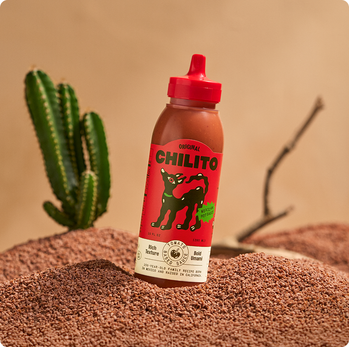 Chilito hot sauce bottle with red cap on a sandy surface with a cactus in the background