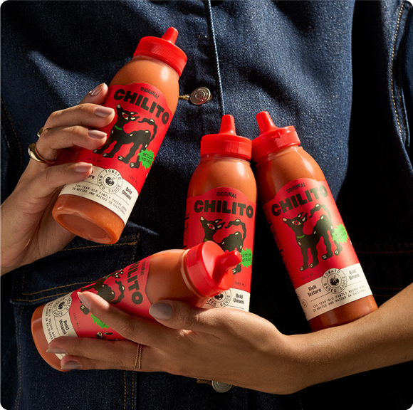 Person holding four bottles of Chilito hot sauce with a denim jacket.