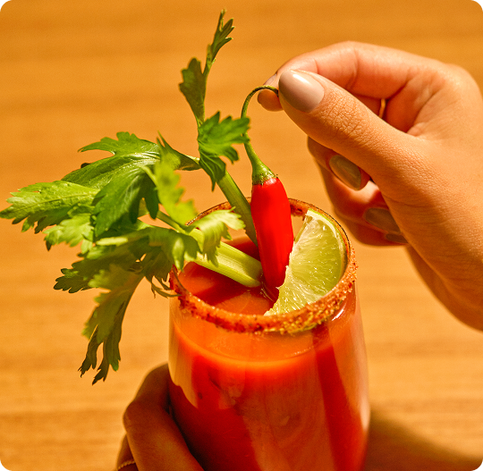 Hand holding a glass of red juice with garnishes on a wooden surface