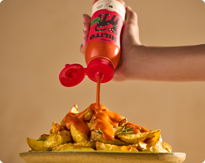 Hand pouring red sauce from a bottle onto a plate of food with a plain background