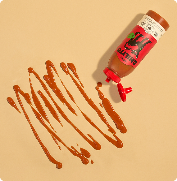 Bottle of hot sauce with a drizzle of sauce on a beige background
