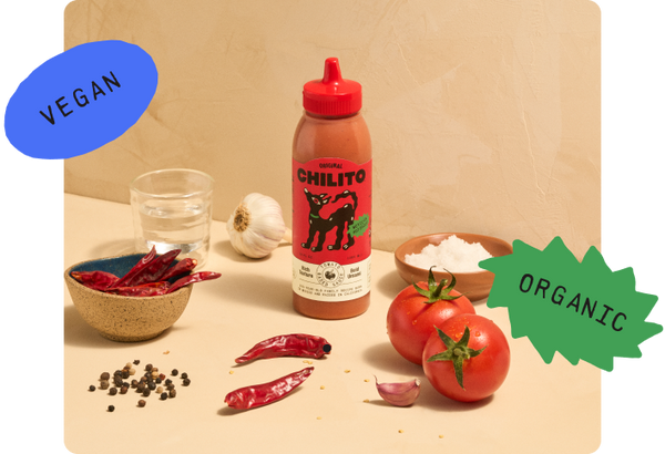 Chilito sauce bottle with organic and vegan labels on a wooden surface with ingredients.