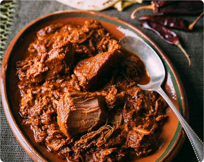 Braised meat in a bowl with a spoon on a textured surface
